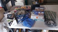 Wide image of most lot items on table showing puzzles, puzzle mat, blue cloth, Lego set in unopened box, and packed pickleball set