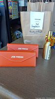 Two orange Joe Fresh sunglass cases displayed on a table with a MaxSold branded paper bag in the background.
