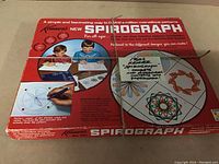 Original box of 1960s Kenner Spirograph game tied with string showing front top cover with graphics and handwritten label describing completeness and condition.