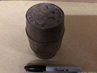 Closed Barrel of Monkeys game barrel with engraved game logo and date on lid, shown next to Sharpie pen for scale.