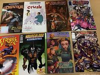 Photo shows 8 different comic books laid out in two rows, titles visible including Cassaur, Crush, Red Sonja, Witchblade, Stryke Force, Youngblood Strikefile, Descendants, and an armored character comic.