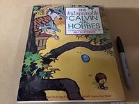 Front cover photo showing the title 'The Indispensable Calvin and Hobbes' with an illustration of Calvin and Hobbes in a treehouse with a yellow background and a black marker for size scale.