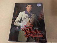 Full cover of The John Travolta Scrapbook showing the signed autograph by John Travolta on the white suit jacket.