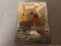 Close-up photo of a Pikachu V Pokemon card with a gold special design, showing card details, image, and text.
