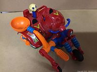 Front and side view of the red, orange, and blue Madballs Rollercycle toy showcasing skull figure and decals.
