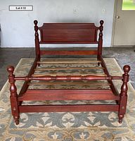 Front view of full-sized cherry wood bed frame showing headboard, footboard with cannonball finials, side rails, and wood slats