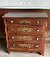 Front view of four drawer chest with floral stencil, ceramic knobs, scalloped skirt and wood finish.