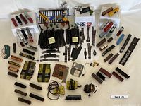 Overhead photo showing a variety of HO scale train cars, engines, track sections, transformers, power packs, and assorted train accessories including scenery items like trees and buildings.