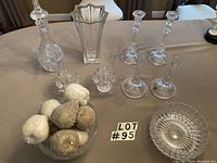Wide shot showing wine decanter with stopper, large vase, two crystal votives, two sets of candlesticks, and a bowl with decorative fruit.