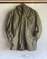 Full front view of green vintage men's rugged field jacket hanging on hanger, showing front pockets and button closure.