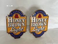 Two matching JW Dundee's Honey Brown Light metal beer signs side by side on a white background.