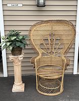 Front full view of wicker peacock chair next to ceramic pedestal with faux plant