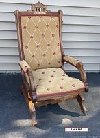 Front view of the antique wooden platform spring rocker, showing gold and terra cotta diamond tufted upholstery, carved wood frame and base with caster wheels on front legs.