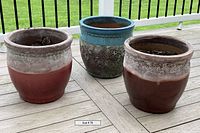 Three large terra cotta pots displayed on a wooden deck, showing their distinctive glazes and shapes.