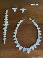 Full view of vintage collar necklace, bracelet, and clip earrings made of white carved shell pieces.