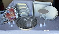 Wide view of all items including various shaped cake pans, plastic couplers, clear cake riser, and cookbook holder