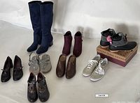 All eight pairs of footwear arranged on floor including boots, booties, slippers, sneakers, and heels