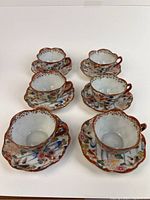 Set of six porcelain cups with matching saucers, showing hand painted chrysanthemum and koi fish designs, scalloped rims, reddish-brown accents, all in excellent condition.