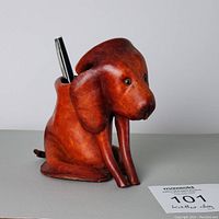 Front and side view of a brown leather dog-shaped holder with pen inserted, showing detailed face and legs of dog.