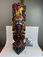 Front view of large hand carved and painted Aztec sculpture with storyteller tile beside it.