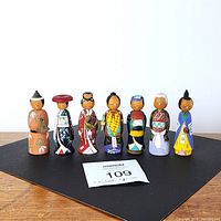 Seven miniature wooden Japanese kokeshi dolls displayed in a row on a black mat