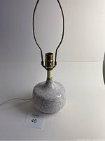Full view of lamp showing crackle glaze ceramic base, brass socket, cream colored neck with brass harp.