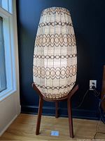 Full view of lamp showing woven shade pattern and three-leg teak base