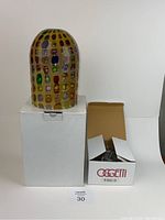 Front view of the multicolored Venetian glass pendant light showing the dome shape and colorful glass pattern, sitting atop a white box with the original hardware box next to it.