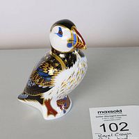 Front-and-right profile of puffin showing painted feathers and fish motif