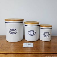 Three white ceramic canisters with blue Dansk Bistro markings and wooden lids on wooden surface.