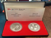 Two silver medallions in protective capsules displayed inside a red velvet-lined case. Informational card with bilingual text from Royal Canadian Mint placed in the back.