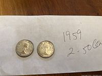 Two 1959 Canadian 50 cent coins on white cloth, obverse side with Queen Elizabeth II profile.