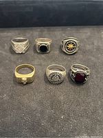 Photo displaying all six silver rings arranged in two rows on a black mat, showing clear details of the design on each ring.