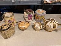 Lot overview showing six ceramic vessels including jars and teapots on a surface