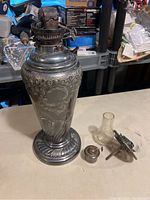 Full view of the antique oil lamp body with separate parts including glass chimney, wick mechanism and burner cap on table