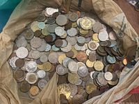 Plastic bag filled with a large pile of assorted world coins in various metals and shapes