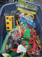 Top-down view of box with power strips, surge protector packaging, jumper cables, paint brushes, clamps, and batteries.