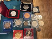 Top-down view of various commemorative coins and medals laid out on a surface, showing different sizes, materials, and presentation cases.
