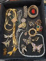 Overview of all jewelry items in the lot within a black display tray, showing mix of brooches, necklaces, bracelets, and earrings.
