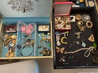 Top view of two jewelry boxes filled with assorted earrings, brooches, necklaces, and pins.