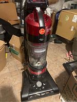 Front view of the red and black Hoover upright vacuum with clear dust collection canister, showing WindTunnel Rewind Plus label and control dial.