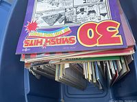 Top down image of a blue bin containing a stack of vinyl records, showing several album covers with colorful and illustrated designs.