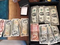 Photo showing a mix of Canadian one and two dollar bills, as well as U.S. one and two dollar bills arranged in a box and on a table.
