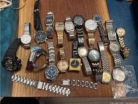 Top down photo showing 17 watches in assorted styles and band materials laid out on wooden surface.
