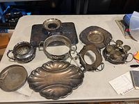 Photo of silver plated items arranged on a table with visible tarnish and wear, showing large scalloped tray, sugar bowl, small trays, and accessory pieces.