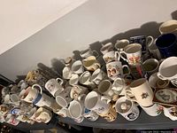 Wide shot showing various royal-themed ceramic mugs arranged tightly on a table, featuring colorful designs and different sizes.