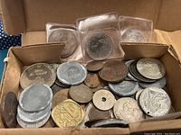 Top view of the coin lot showing a variety of metal coins silver, copper, and gold toned with some in sleeves and others loose inside a cardboard box