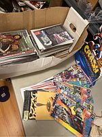 Box of vintage comic books with various issues stacked inside and some loose on table.