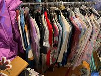 Wide view of the lot showing an assortment of vintage women's clothing on hangers including skirts, dresses, and tops in various colors and patterns.