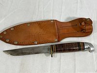 Full view of the hunting knife with leather sheath showing knife handle, blade and sheath construction.